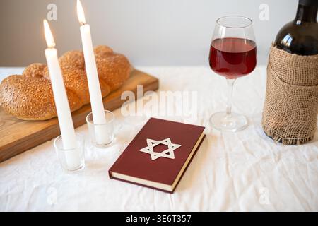 Shabbat Shalom concept. Challah bread, red kosher wine, book and candles on table. Traditional Jewish Shabbat kiddush ritual. Stock Photo