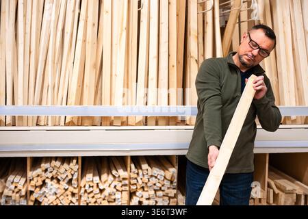 Man selecting timber (wooden bar) for DIY project. Man checking straitness of lumber board in hardware store or wood warehouse. Stock Photo