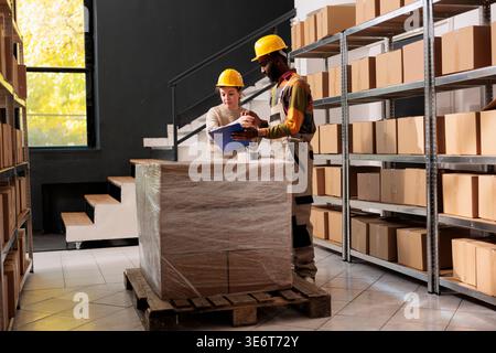 Stockroom colleagues checking merchandise quality control report before start working at customers order in warehouse. Diverse storehouse employees preparing packages for delivey in storage room Stock Photo