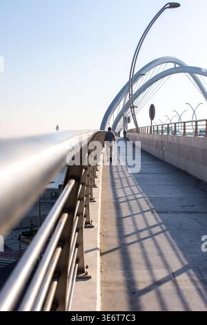 A pedestrian walking on the Infinity Bridge walkway with large metal arches and long shadows in Dubai, UAE. Stock Photo