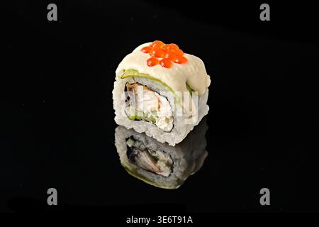 Two sushi rolls wrapped in avocado with grilled eel, cucumber filling, cream sauce and red tobiko caviar on top, isolated on black background with mir Stock Photo