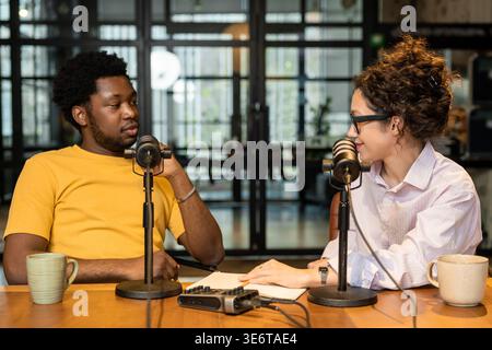 Diverse colleagues recording podcast and talking in microphones Stock Photo