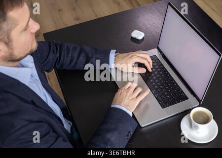 Top view of man typing on laptop at desk with coffee and wireless earbud case in workspace Stock Photo