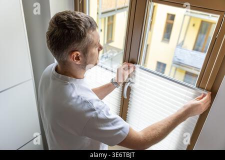 Man installing pleated blinds on window at home interior with natural daylight Stock Photo