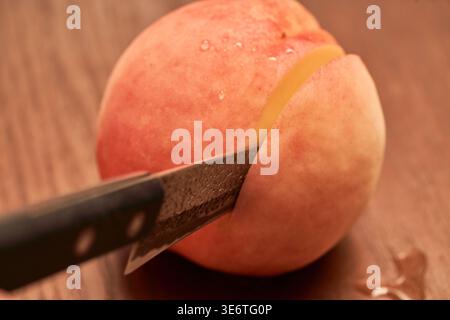 A fresh, juicy peach is sliced with a knife on a wooden board. Glistening water droplets highlight the mouthwatering appeal of this summer fruit. Stock Photo