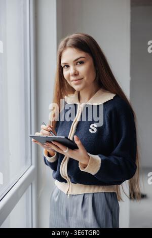 Young female interior designer working on digital tablet with stylus, planning home renovation project by the window. Stock Photo