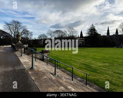 Wide view of a quiet Edinburgh park with green grass, a metal art sign and dramatic skies. Stock Photo