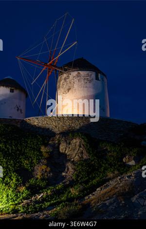 Traditional windmill illuminated at night in Mykonos, Greece. Famous landmark with dramatic dark blue sky. Stock Photo