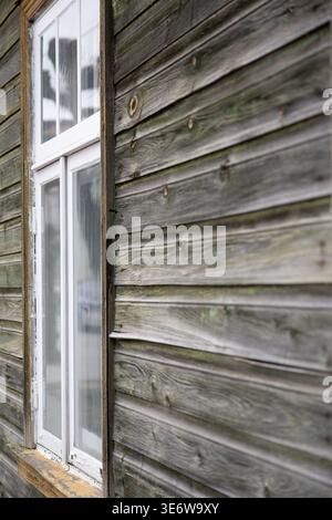 Old wooden house wall with white window, rustic exterior detail Stock Photo