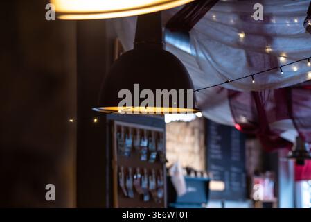 A cozy café interior with warm hanging lights, string fairy lights, fabric ceiling drapes, and a blurry menu board in the background. Stock Photo