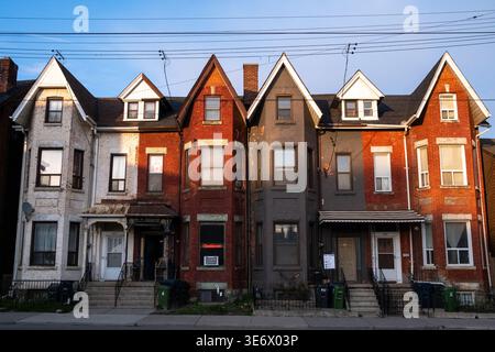 Street view of a row of attached residential houses with brick and painted facades along a sidewalk in Toronto, Ontario, Canada, April 26, 2023. This Stock Photo