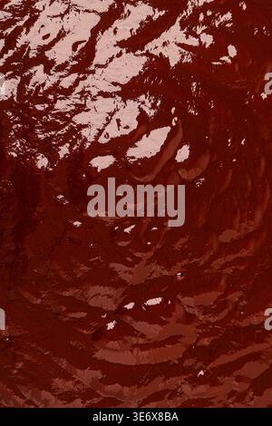 Dark red-brown liquid surface with glossy reflections creating an abstract texture Stock Photo