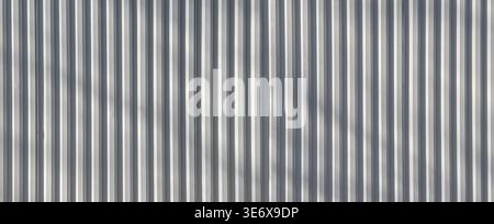 Gray metallic steel siding forming a rhythmic pattern with vertical lines and shadows Stock Photo