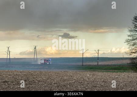 Fire truck moving across a rural area covered in smoke after a grassland fire, emergency response scene in countryside Stock Photo