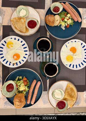 Breakfast table with various dishes including eggs, sausages, salad, bread, and cups of coffee. Mobile photo Stock Photo