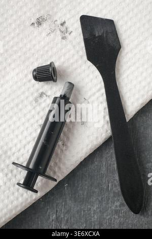 black plastic thermal paste syringe and applicator spatula on white textured paper towel, top view, concept of computer hardware maintenance Stock Photo