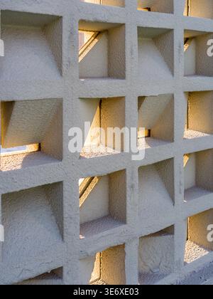 A close-up view of a thick white decorative wall featuring a grid of square perforations, with sunlight casting sharp geometric shadows within the ope Stock Photo