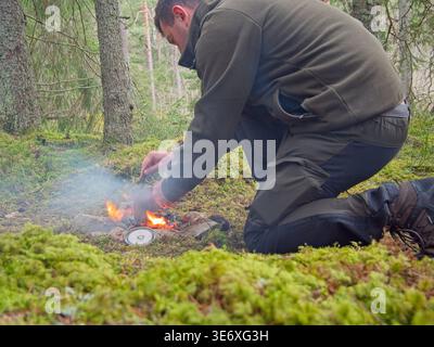 Man lighting campfire during bushcraft camping in forest Stock Photo