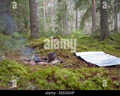 Bushcraft campsite with campfire and sleeping pad in forest Stock Photo