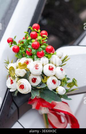 A decorative bouquet with red berries and white flowers attached to a car mirror. The arrangement features green leaves and a red ribbon. Stock Photo