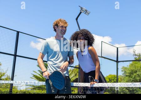 Couple standing at net after rally, holding paddles and taking break in sportswear on paddle court Stock Photo