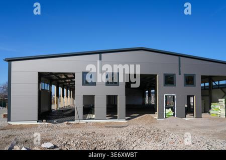 Modern warehouse under construction featuring sandwich panel facade, large openings and unfinished interior on a clear sunny day Stock Photo