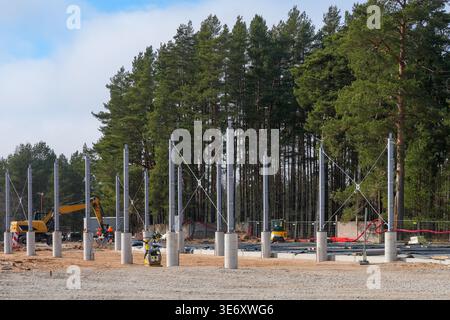 Industrial construction site with steel columns, concrete foundations and heavy machinery set against forest backdrop during early building phase Stock Photo