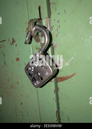 Open Rusty Padlock On Green Door, Hanging From Hasp, Chipped Paint And Heavy Corrosion, Closeup Showing Rough Texture, Shadowed Edges, Industrial Deca Stock Photo