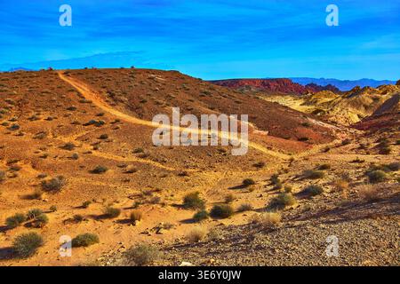 Desert Trail Winding Through Rocky Hills And Red Rock Formations Under Blue Sky Stock Photo