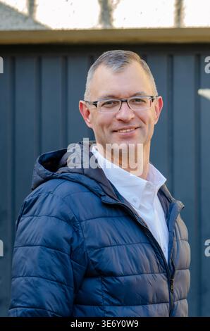 Man wearing glasses smiles outdoors in jacket and looks at camera. Stock Photo
