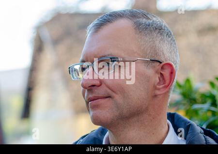 Close up profile portrait of fifty year old man wearing glasses outdoors with blurred background in natural daylight. Stock Photo