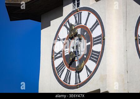 View of the vibrant clock tower stands tall against the bright blue sky, its golden hands a stark contrast to the white stone, Graz, Styria, Austria. Stock Photo