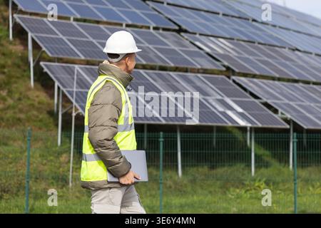 A young electrical engineer examines solar panel installations while using a laptop in a renewable energy environment. Stock Photo