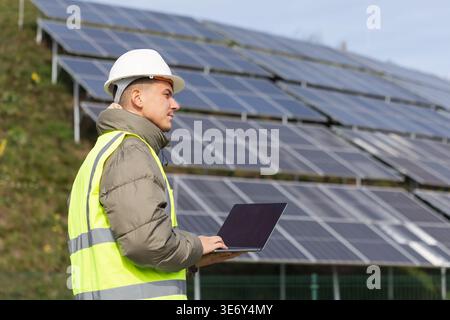 A young male electrical engineer inspects solar panel systems with a laptop in a renewable energy setting. Stock Photo