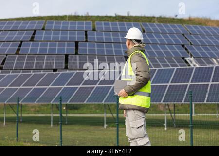 A young male electrical engineer inspects solar panel systems and manages installations while using a laptop in a renewable energy area. Stock Photo