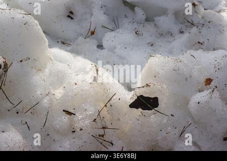 Gritty, melting snowdrift along roadside. Chunky ice and mud create a stark winter-to-spring transition. Raw textures of slushy dirty snow, late seaso Stock Photo