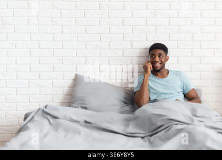Smiling black man talking on mobile phone in bed Stock Photo