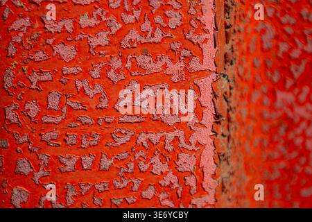 View of peeling, vibrant red paint on a textured surface creates an abstract landscape of color and decay, Dronten, Flevoland, Netherlands. Stock Photo
