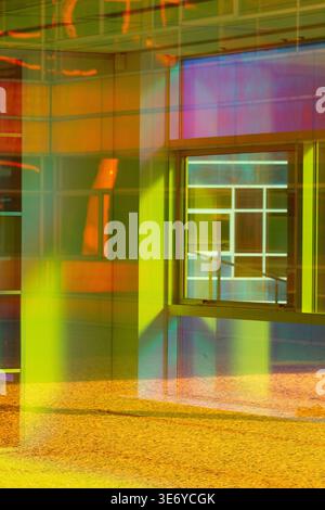 View of vibrant yellow and green glass panels create a kaleidoscopic facade with a window reflecting light, casting shadows on the ground, Almere, Fle Stock Photo