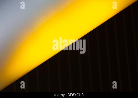 View of a stark contrast where bright yellow light dramatically intersects with a deep black textured surface and a soft grey area, La Defense, Flevol Stock Photo