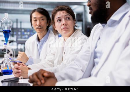 Diverse team of lab scientists inspecting clarity of chemical solution in glass flasks for purity verification. Teamworking research facility coworkers prepare reagent containers for assay procedures Stock Photo
