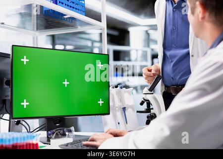 Green screen on desktop pc with two scientists working in chemistry lab, clinical research emphasizes molecular biology, healthcare innovation and biotechnology research for discovery. Stock Photo