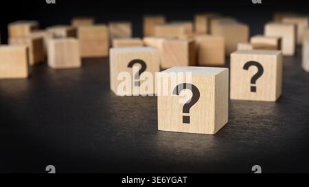 Question marks on wooden blocks with blurred scattered cubes. FAQ, uncertainty and problem solving concept on dark background. Stock Photo