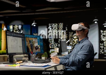 Interior designer using virtual reality headset to create a floor plan, working on apartment layout with architectural software and blueprints. VR glasses and CAD modeling program. Stock Photo