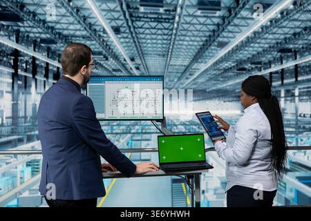 Green screen laptop used by hardware developers designing microchip layout with EDA program in industry 4.0 plant. Workers review automated semiconductors smart factory schematics with mockup notebook Stock Photo