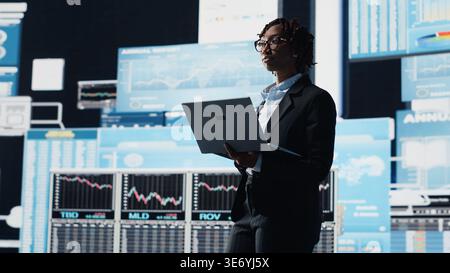 Business specialist using laptop to compare company KPIs data on digital videowall before making decisions. Leader analyzing enterprise corporation key performance indicators using notebook, camera B Stock Photo
