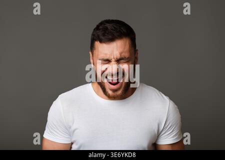 Young man in white t-shirt grimacing and crying Stock Photo