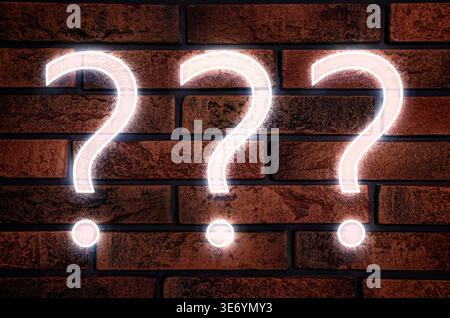 Three glowing question marks on brick wall Stock Photo