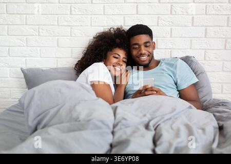 Happy couple cuddling in bed with smartphone Stock Photo