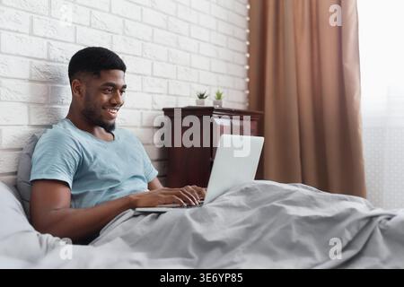 Black man in bed working with laptop Stock Photo